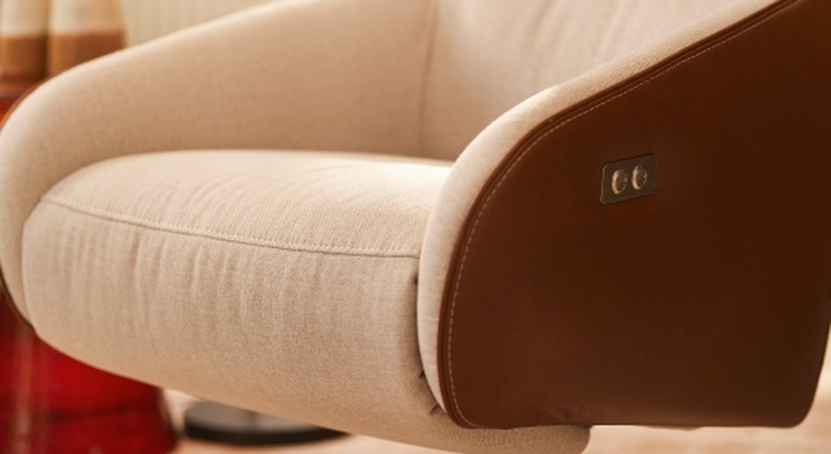 Close-up of a beige armchair with brown leather sides, featuring a small control panel, set against a blurred background.