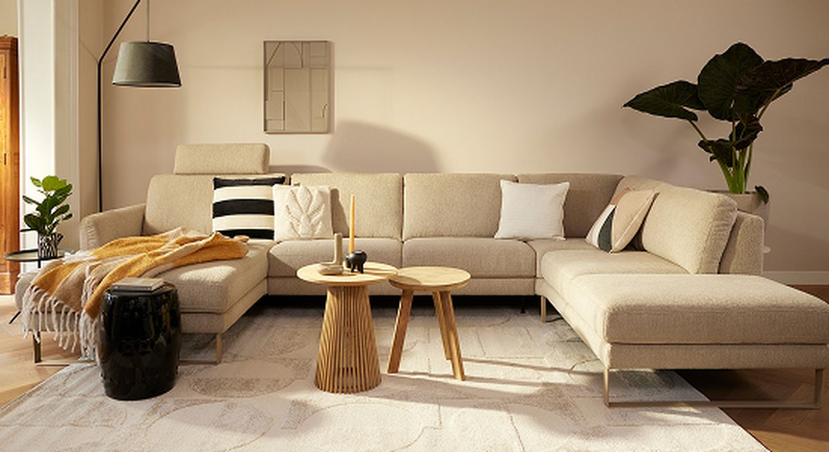 Modern living room with a beige sectional sofa, striped and white pillows, a mustard throw, a wooden coffee table, plants, and decorative accents.