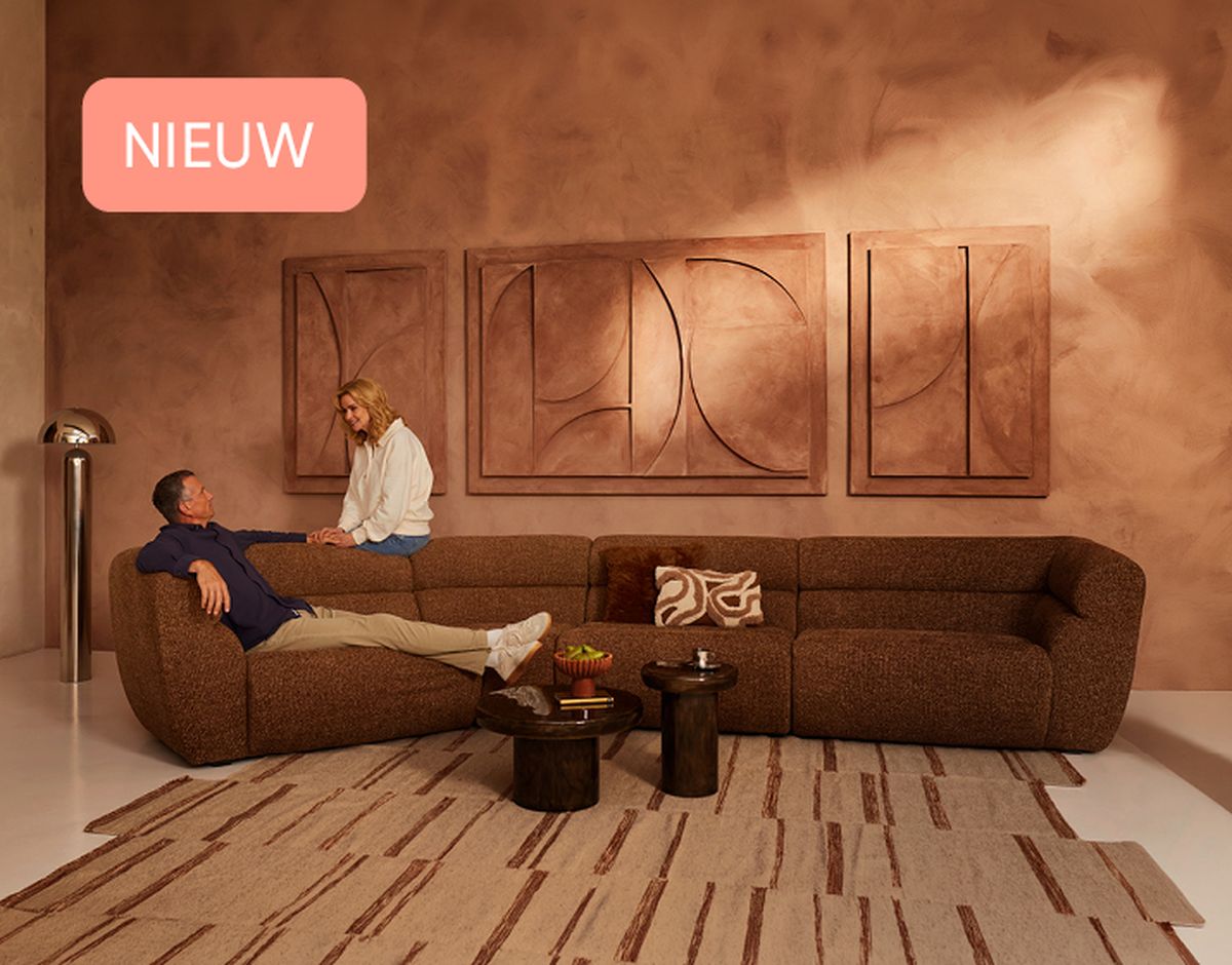 A man reclines on a brown sectional sofa, talking to a woman sitting beside him in a cozy, art-adorned living room with a contemporary design.