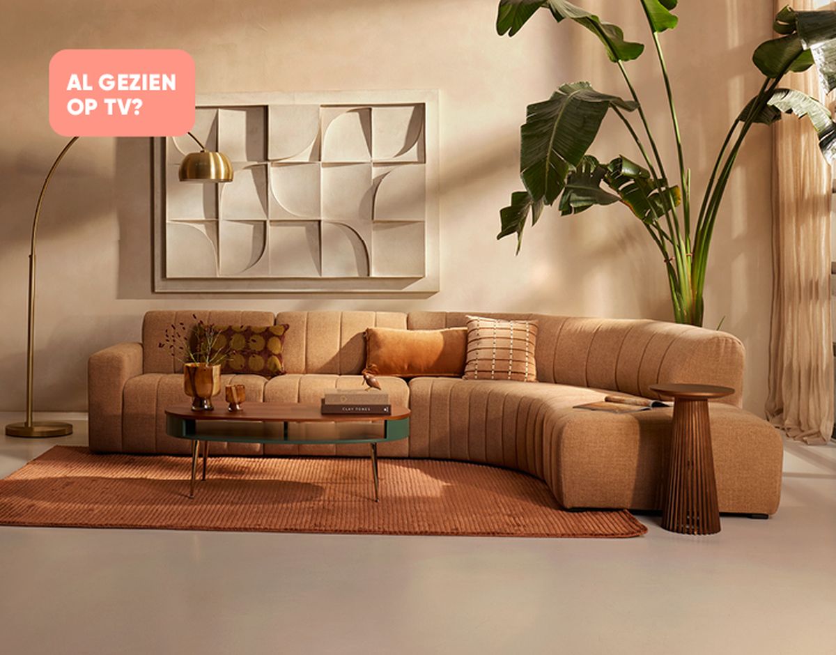 Stylish living room with a curved beige sofa, round coffee table, modern artwork, floor lamp, large plant, and warm-toned decor.