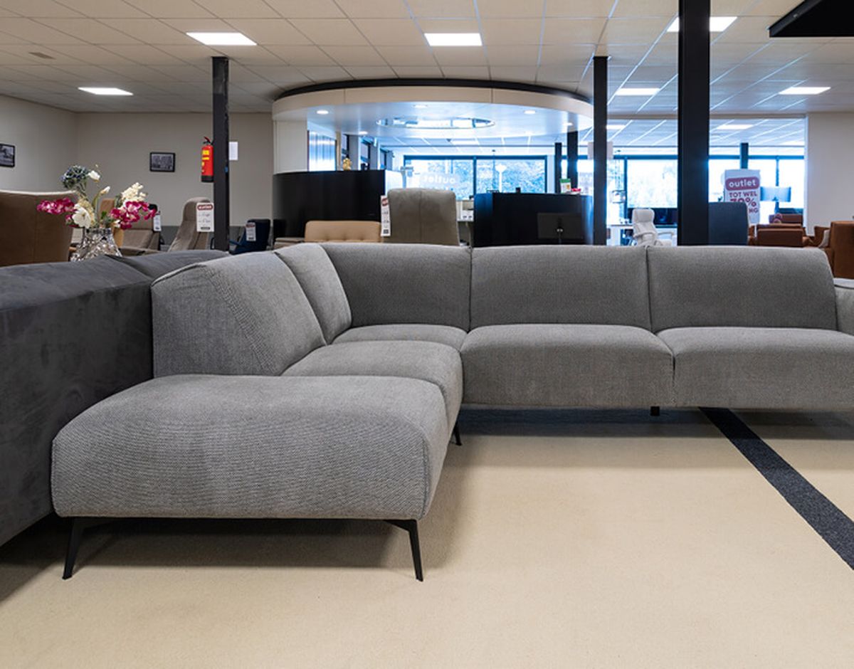 A modern furniture showroom featuring a large gray sectional sofa with black legs, surrounded by other furniture pieces and decor items.