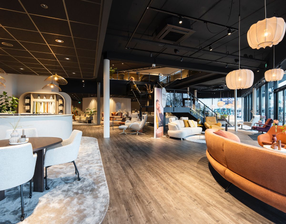 Moderne meubelwinkel met houten vloeren, zitbanken, verlichting en stoelen. Ruime open indeling met hoge plafonds en grote ramen.