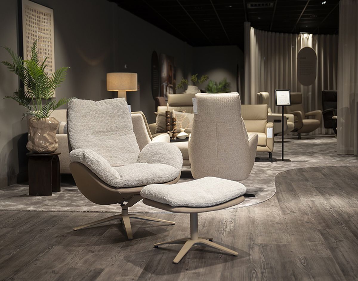 Moderne woonkamer met een stijlvolle fauteuil, bijpassende voetenbank, houten vloer en sfeerverlichting.