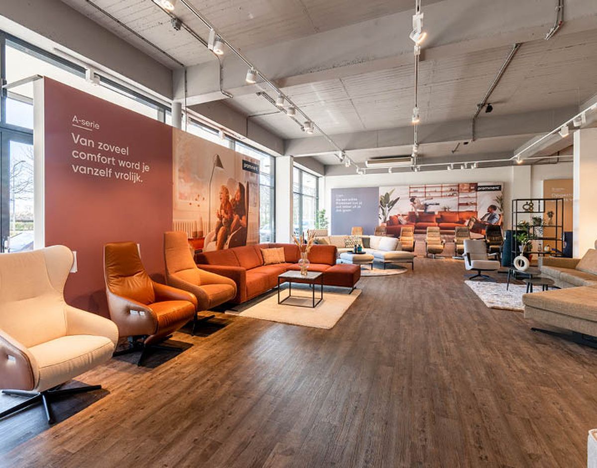 Moderne showroom met diverse comfortabele banken en stoelen, houten vloer en grote ramen die veel natuurlijk licht binnenlaten.