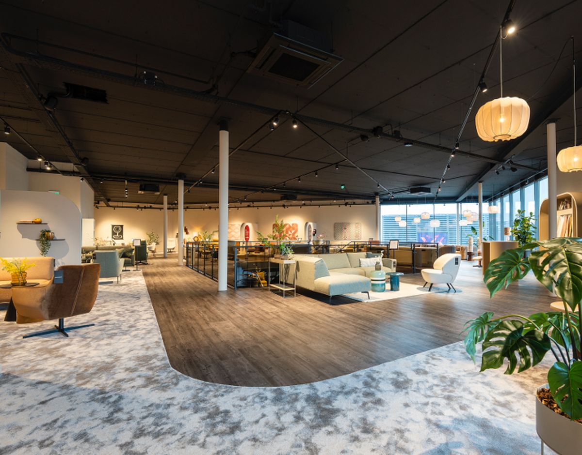 Grote moderne showroom met diverse meubels, waaronder banken en stoelen, met veel verlichting en grote ramen aan de rechterkant.