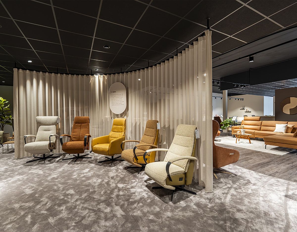 Een showroom met verschillende fauteuils in diverse kleuren, elk met een bijbehorend label, tegen een achtergrond van gebogen gordijnen.
