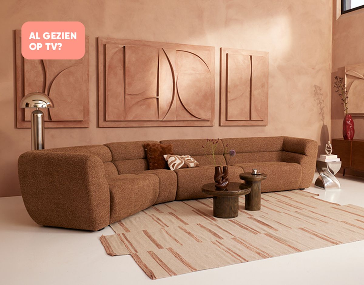 Cozy living room with a brown, curved sofa, abstract wall art, modern side tables, and a patterned rug in a warm, minimalist setting.