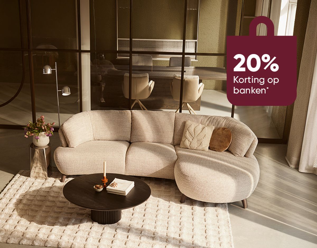 Modern living room with a curved beige sofa and round coffee table on a cream rug. A sign reads "20% Korting op banken."