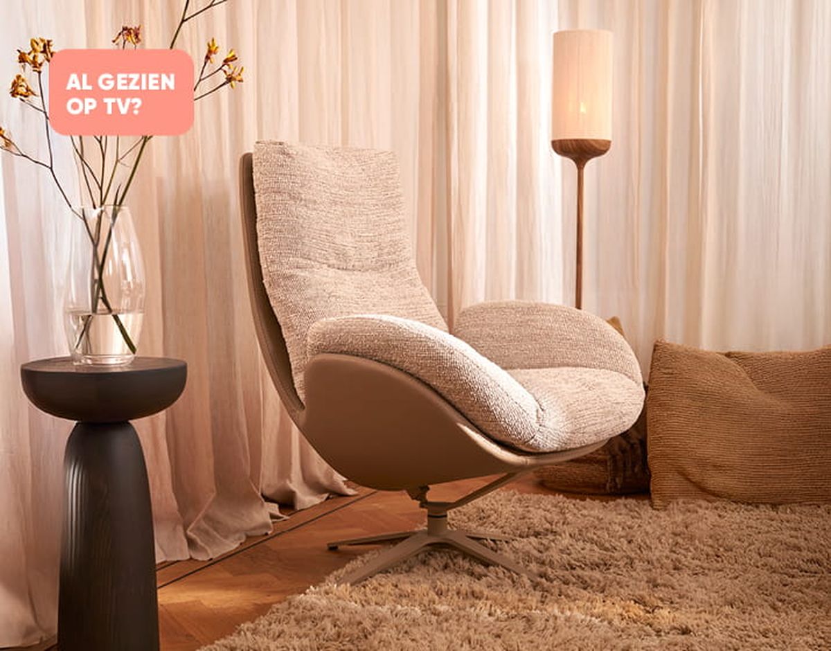 Moderne woonkamer met een comfortabele draaifauteuil, een zwarte bijzettafel met bloemen, en een staande lamp. Warme, neutrale tinten.