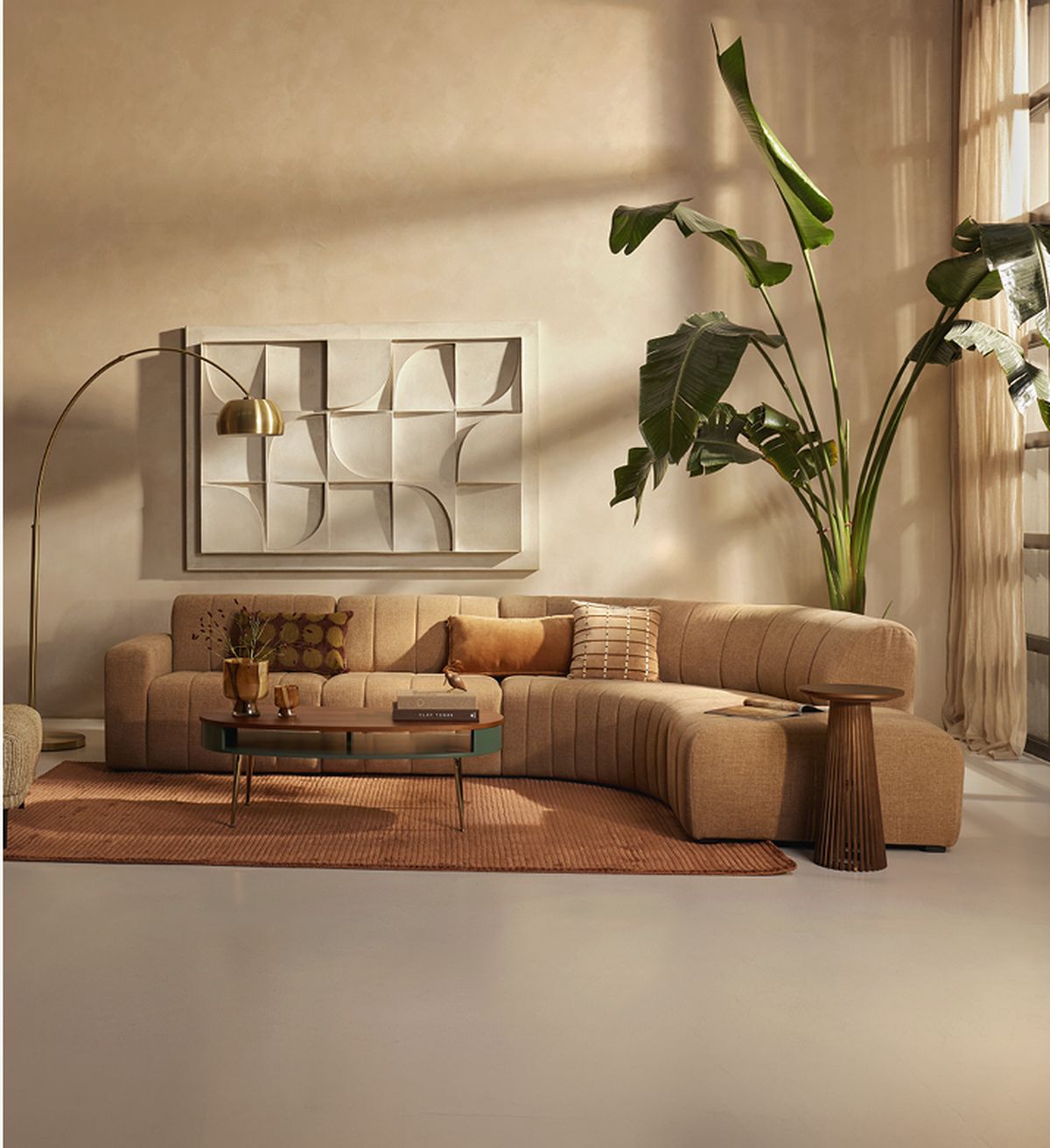 A cozy living room with a beige sectional sofa, decorative pillows, a large plant, and modern wall art. A coffee table and floor lamp add elegance.