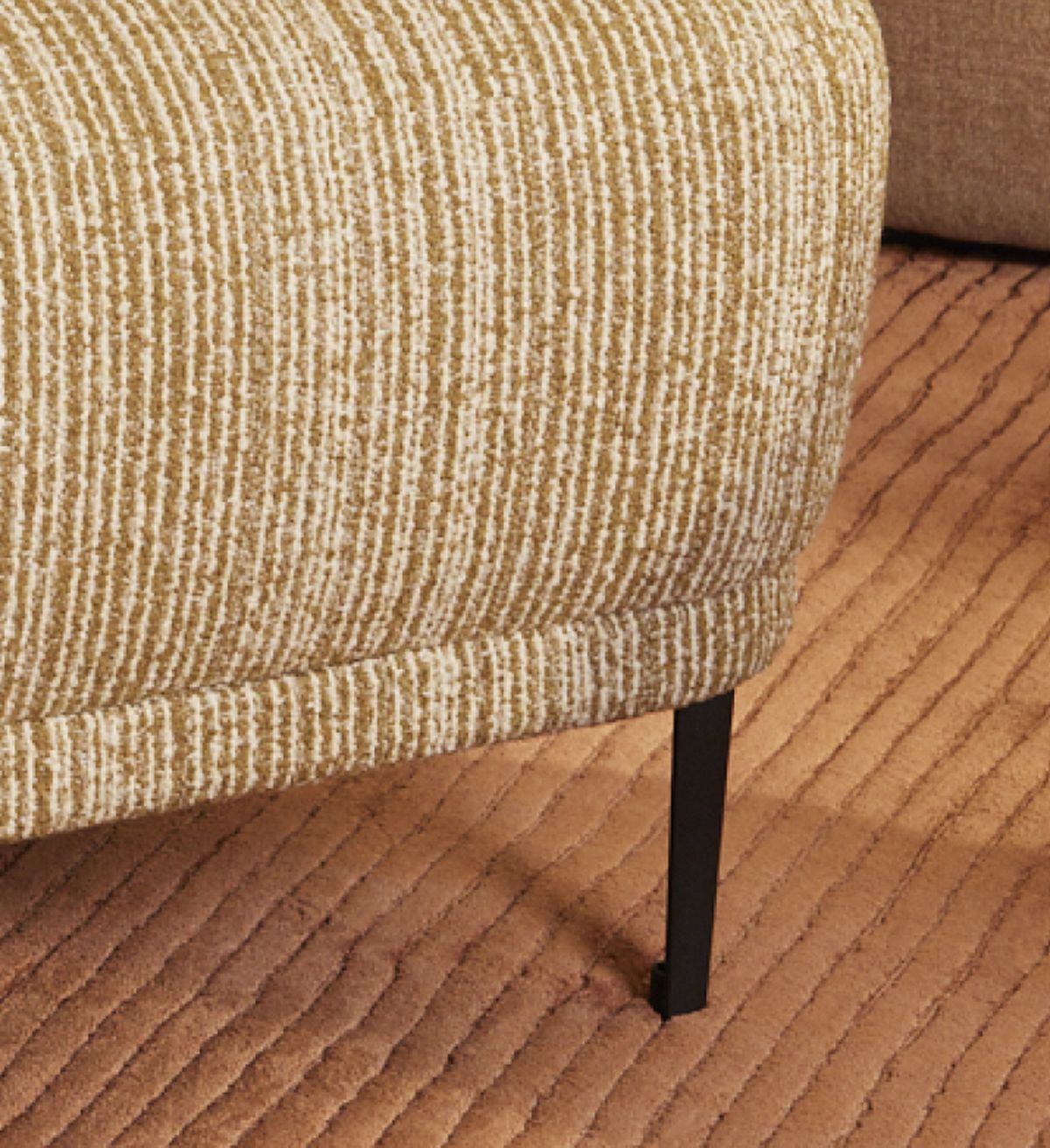 A textured cushion with a striped design sits atop a black metal leg on a ribbed, peach-colored carpet.