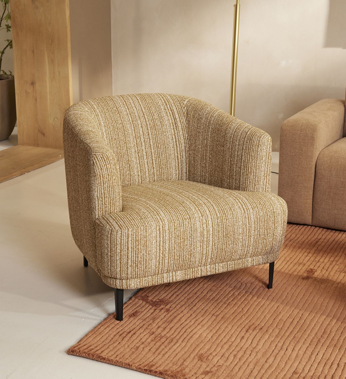 A cozy armchair with striped beige upholstery and black legs on an orange textured rug in a warmly lit room.