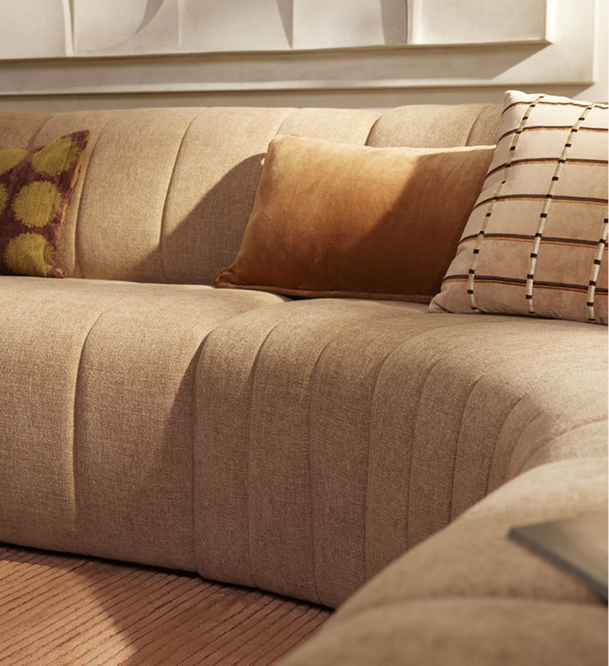 Beige sectional sofa with plush cushions in warm tones, featuring geometric and patterned designs, set in a cozy, softly lit room.