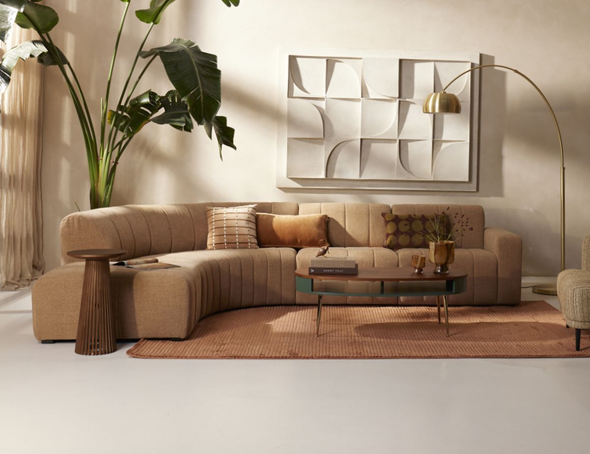A modern living room with a beige L-shaped sofa, decorative pillows, a wooden coffee table, abstract wall art, and a large leafy plant.