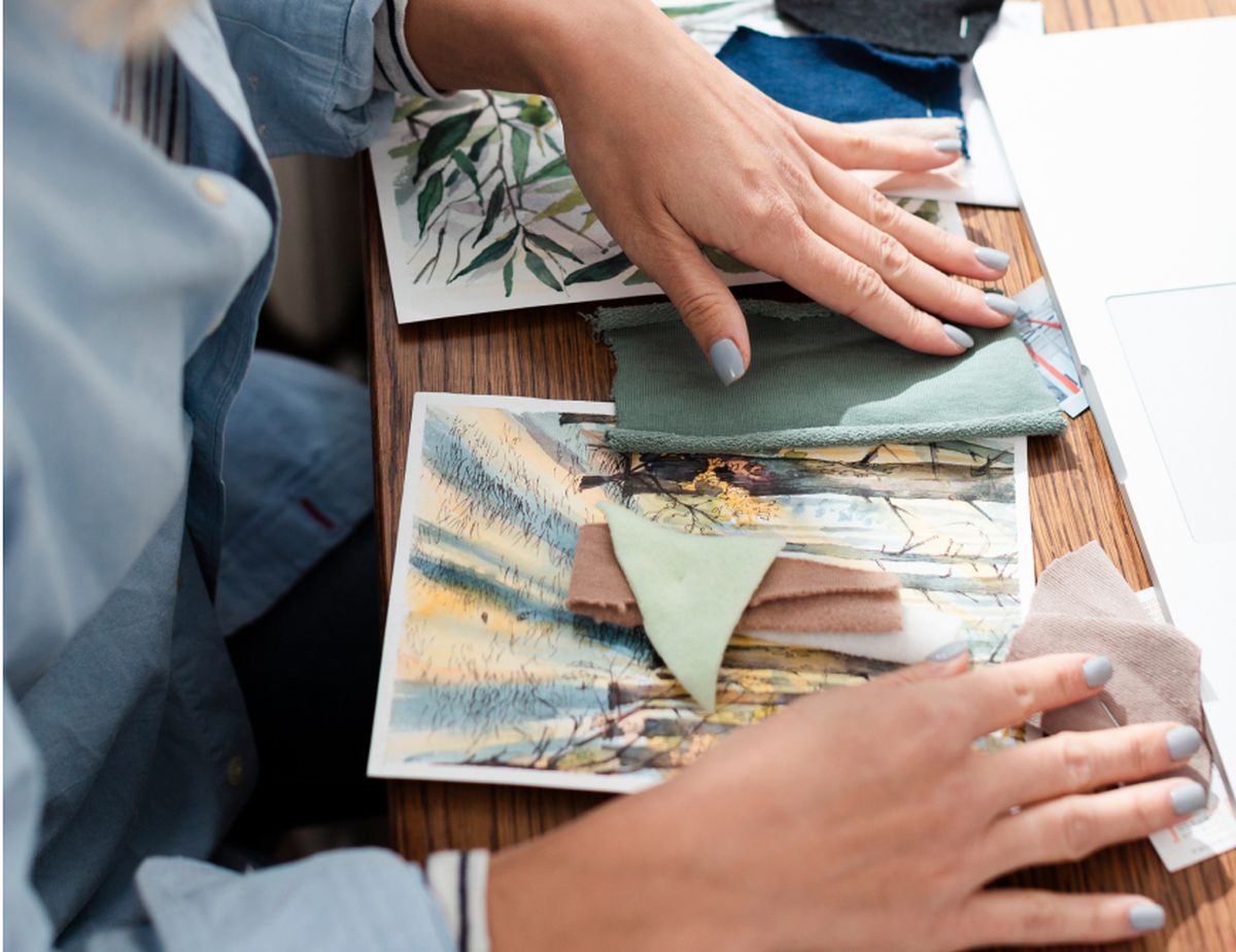 Personenhand selecteert stofstalen en afbeeldingen op een houten tafel, waarschijnlijk voor een ontwerp- of knutselproject.