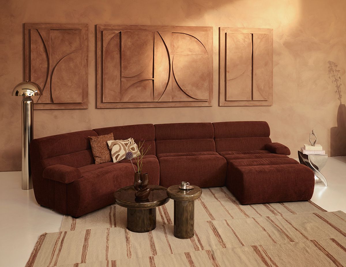 A modern living room with a brown sectional sofa, abstract wall art, vintage floor lamp, wooden side tables, and a patterned rug on the floor.