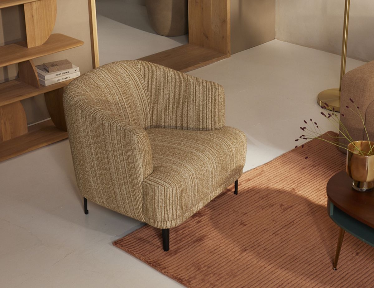 A cozy, beige armchair with striped upholstery sits on a rust-colored rug in a modern, minimalist living room with wooden shelves and decor.