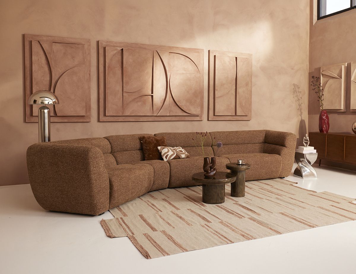 A modern living room with a curved brown sofa, patterned rug, abstract wall art, and two round coffee tables.