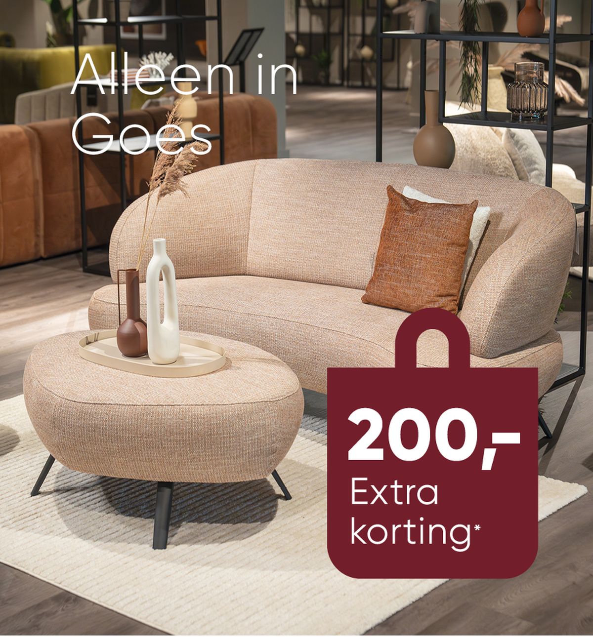 Een beige bank en bijbehorende voetenbank, voorzien van decoratieve vazen ​​in een moderne showroom; inclusief een korting van 200 euro, met het label "Alleen in Goes."
