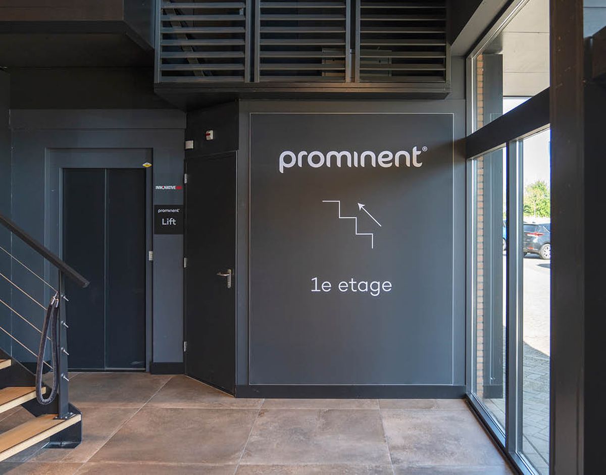 Interieur van een modern gebouw met een lift en trap naar de eerste verdieping, met de tekst "prominent" op de muur.