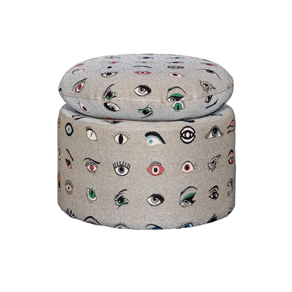 Olympia pouf in round shape, upholstered in a silver-grey fabric patterned with embroidered multicolored eyes in various styles and expressions, topped with a matching round cushion.