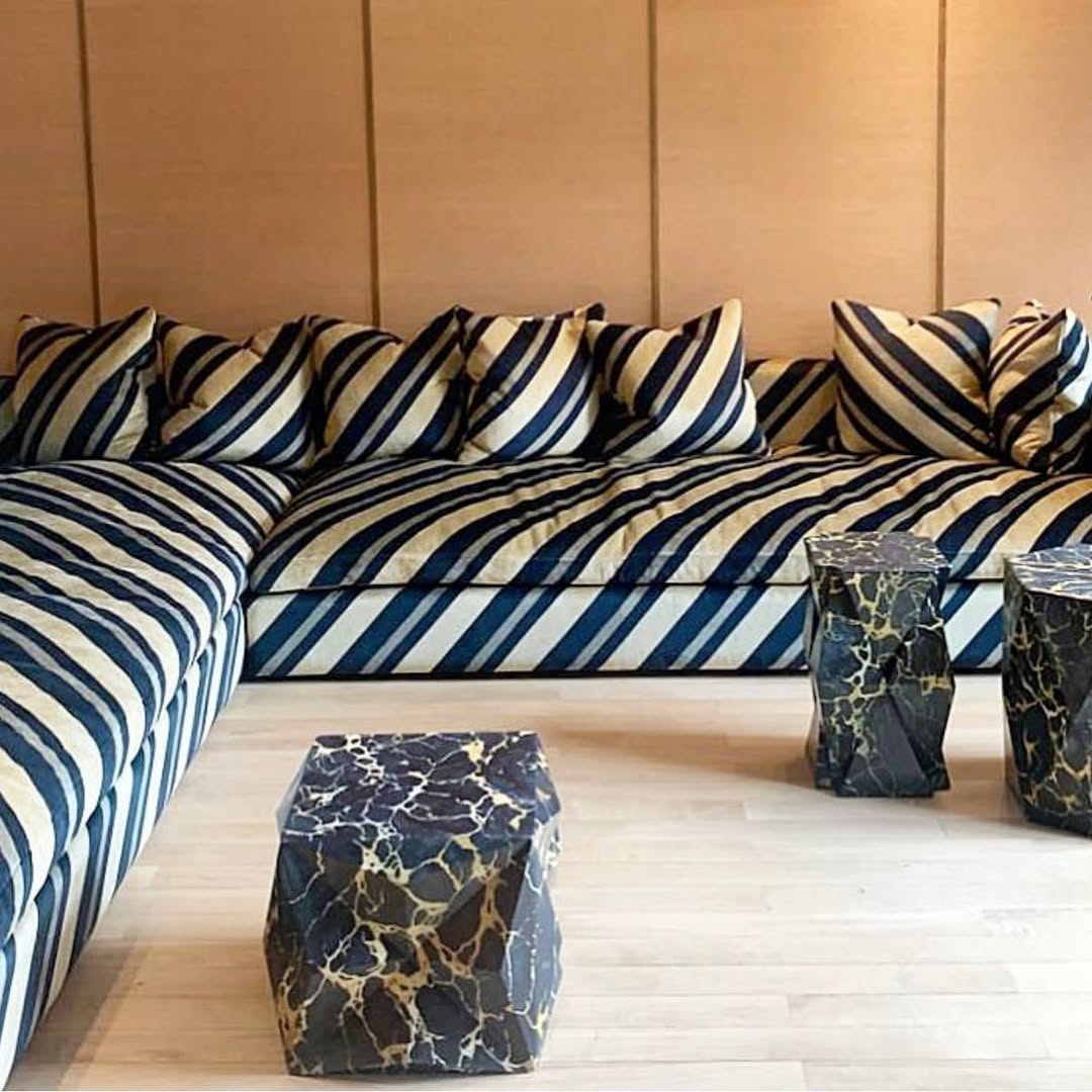 Collett & Victor Trancoso sofa with bold navy and cream diagonal stripes and matching cushions, paired with sculptural marble side tables in a modern living space.