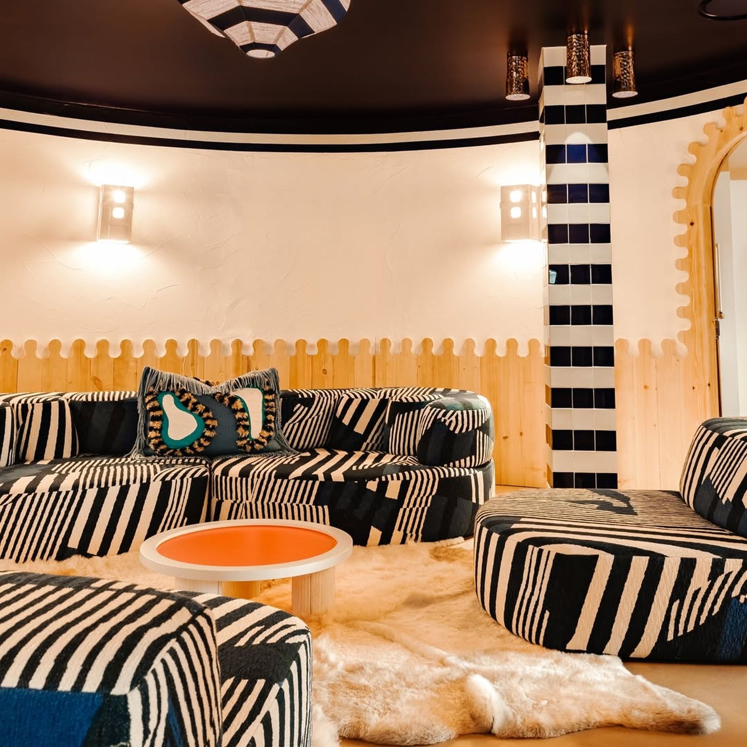 Vibrant JNcQUOI Comporta interior with bold striped modular sofas, playful patterns, and warm lighting creating a stylish and cozy lounge atmosphere.