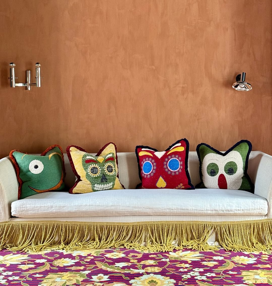 New York sofa with colorful owl-shaped cushions on a fringed base, set against a terracotta wall, with a floral rug underneath.