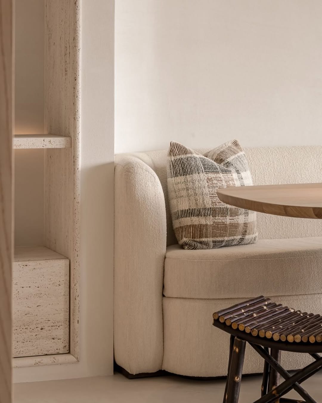 Close-up of the Toscana fixed seat sofa by Collett & Victor in textured cream fabric, styled with patterned throw pillows beside a natural wood dining table and rustic stool in a serene coastal retreat interior.