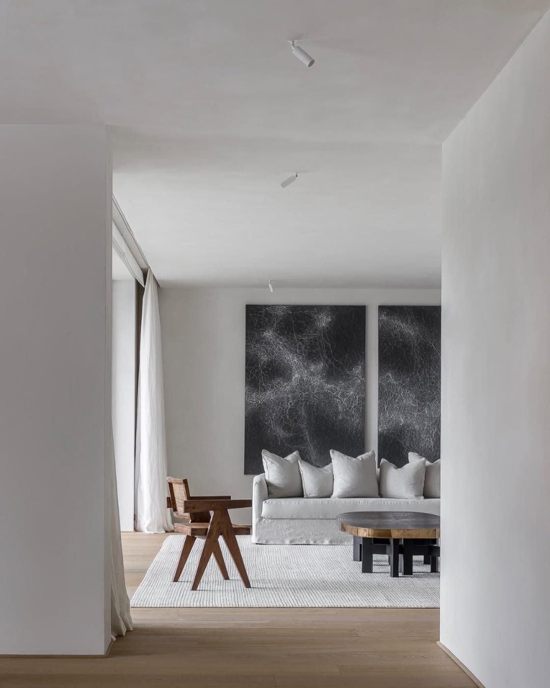 Minimalist living room with the Felix sofa in light fabric, styled with large abstract black wall art, a wooden chair, and a round coffee table on a textured rug.