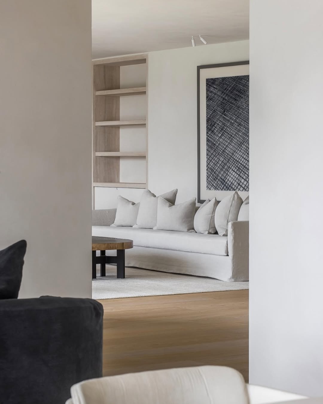 Felix sofa in light neutral fabric with multiple scatter cushions, framed by minimalist shelving and abstract wall art in a serene modern living space.