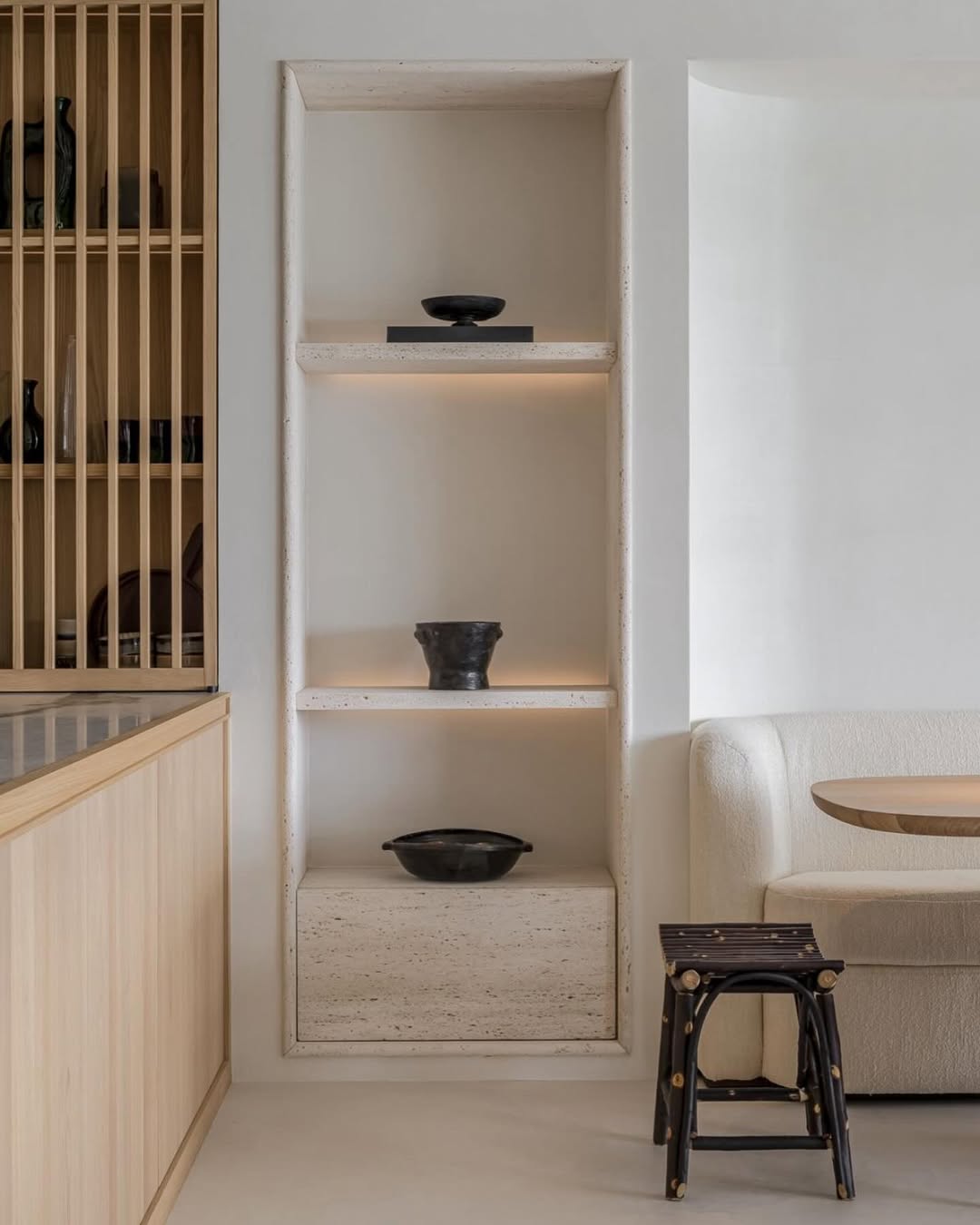 Minimalist shelving detail with ceramic accents, light wood cabinetry, and the Toscana fixed seat sofa by Collett & Victor, styled with a natural wood dining table and dark rustic stool in a serene coastal retreat.