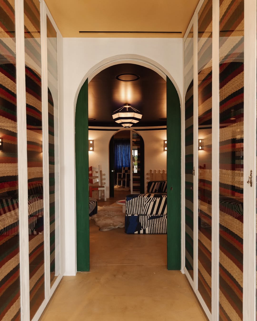Playful hallway at JNcQUOI Comporta leading into a vibrant lounge with bold striped sofas, arched doorway, and eclectic design details blending color and texture.