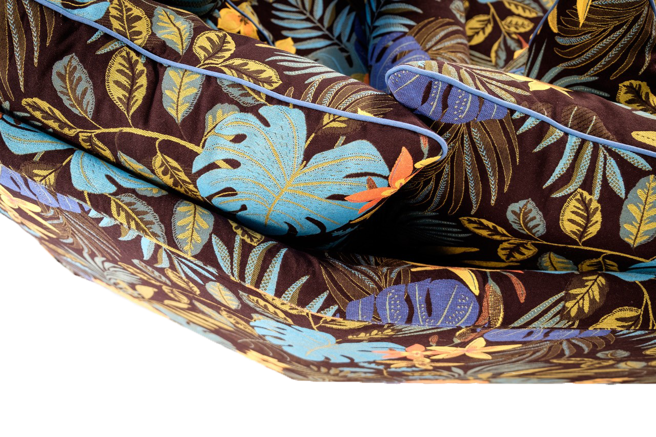 Close-up of the Chacha sofa’s upholstery in a bold tropical fabric, featuring blue, yellow, and orange botanical motifs with contrast piping on the cushions.