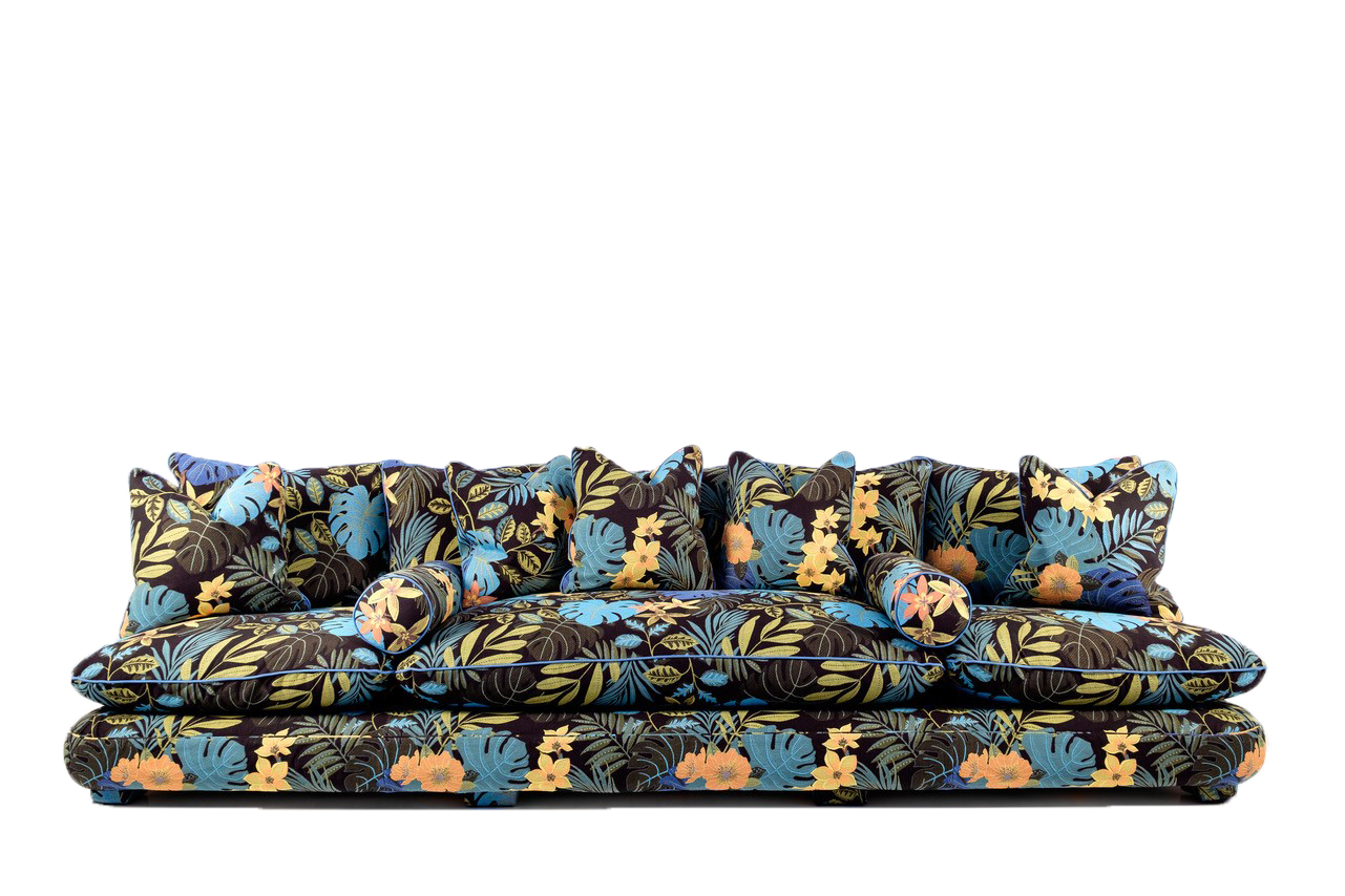 Chacha sofa upholstered in a bold tropical floral fabric with vibrant blue, yellow, and orange leaves and flowers, featuring deep cushions, multiple matching pillows, and two bolster cushions for a playful and eclectic look.