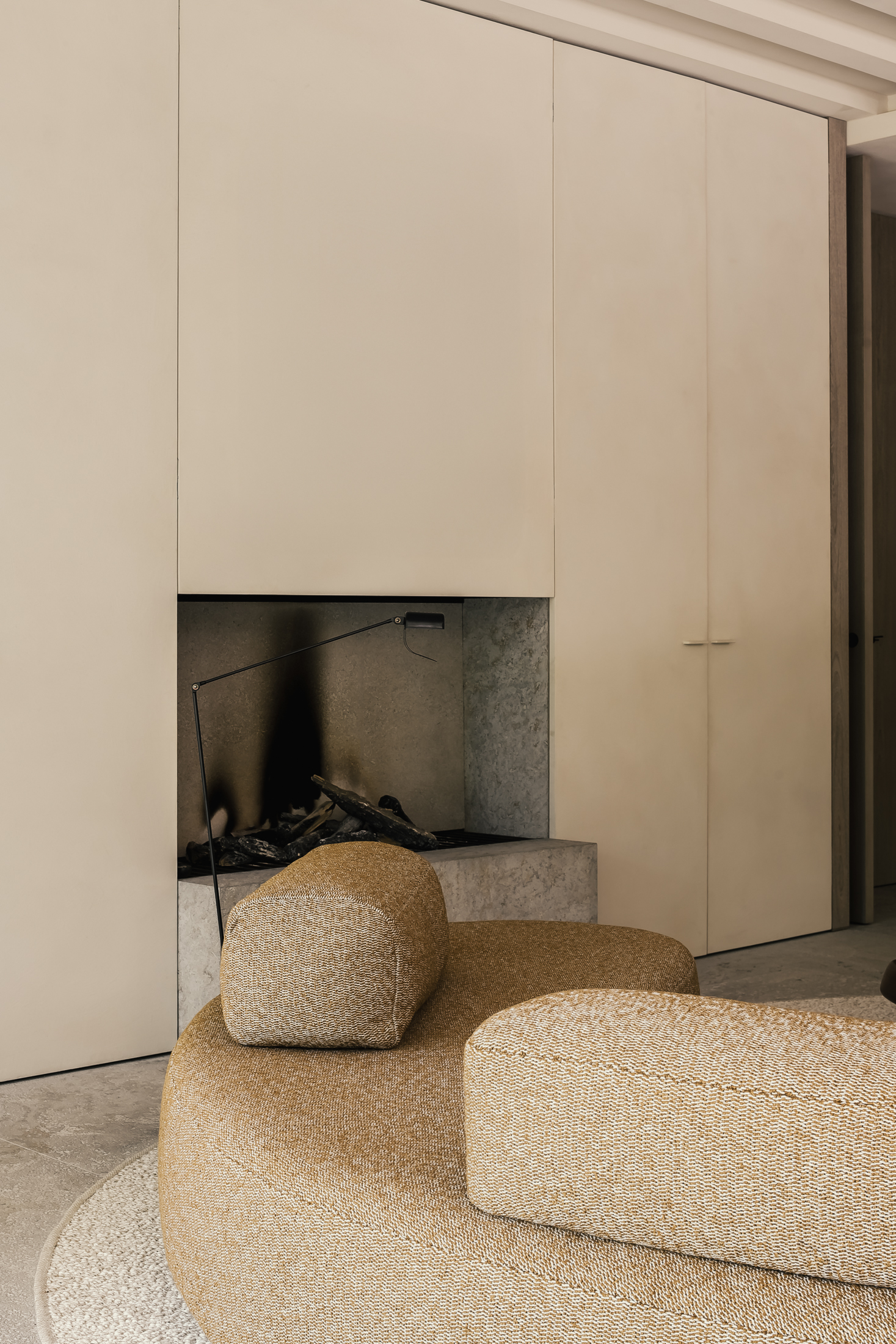 Minimalist living room with a modern beige curved sofa and a sleek, built-in fireplace set against a smooth, light-colored wall.