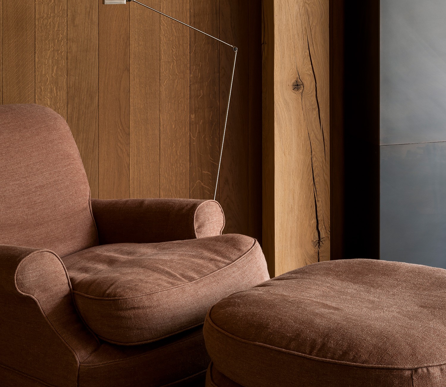 Brown clara one-seater with loose seat and matching ottoman in a wood-paneled room.