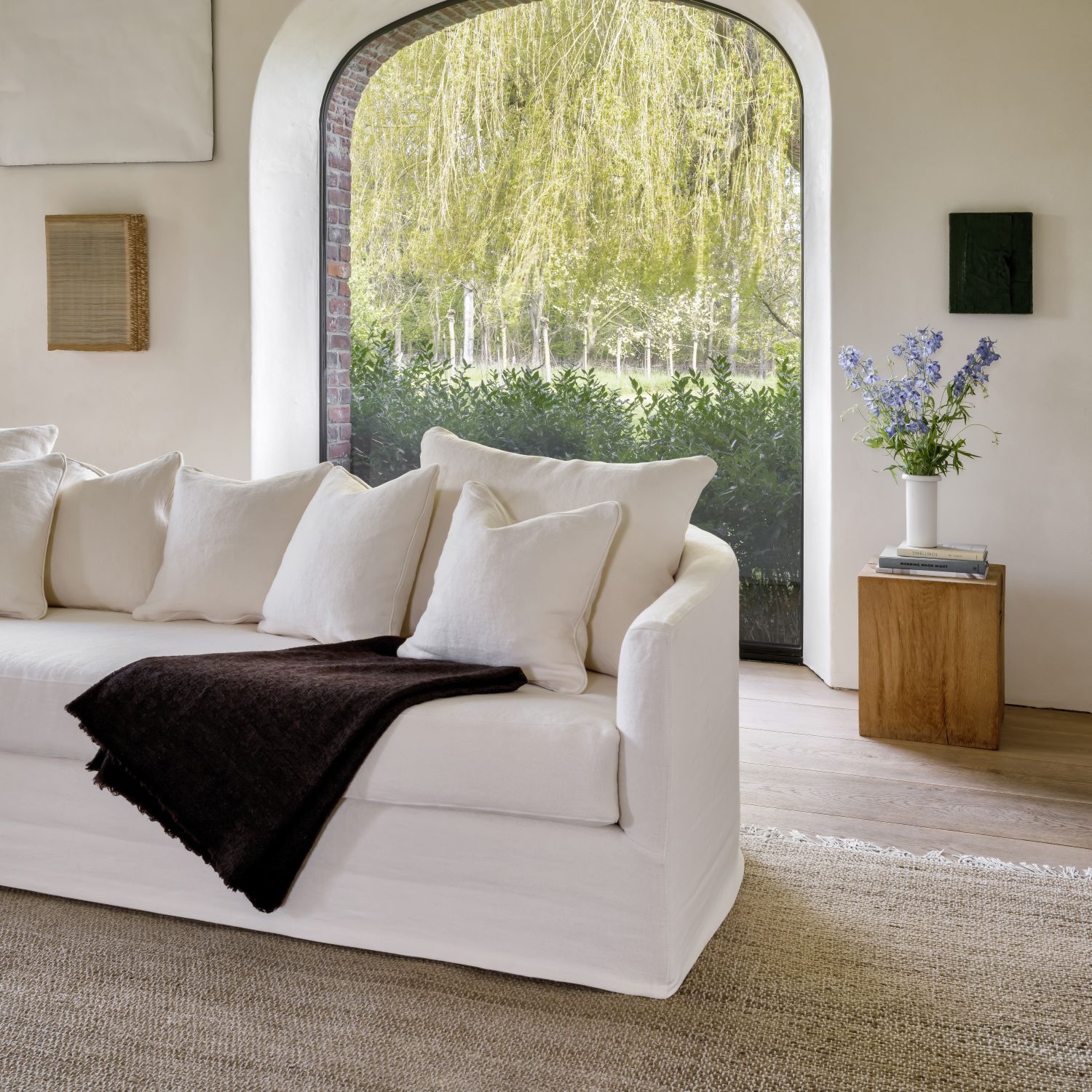 Felix sofa by Collett-Victor in white linen with cushions, styled in minimal living room with large arched window.