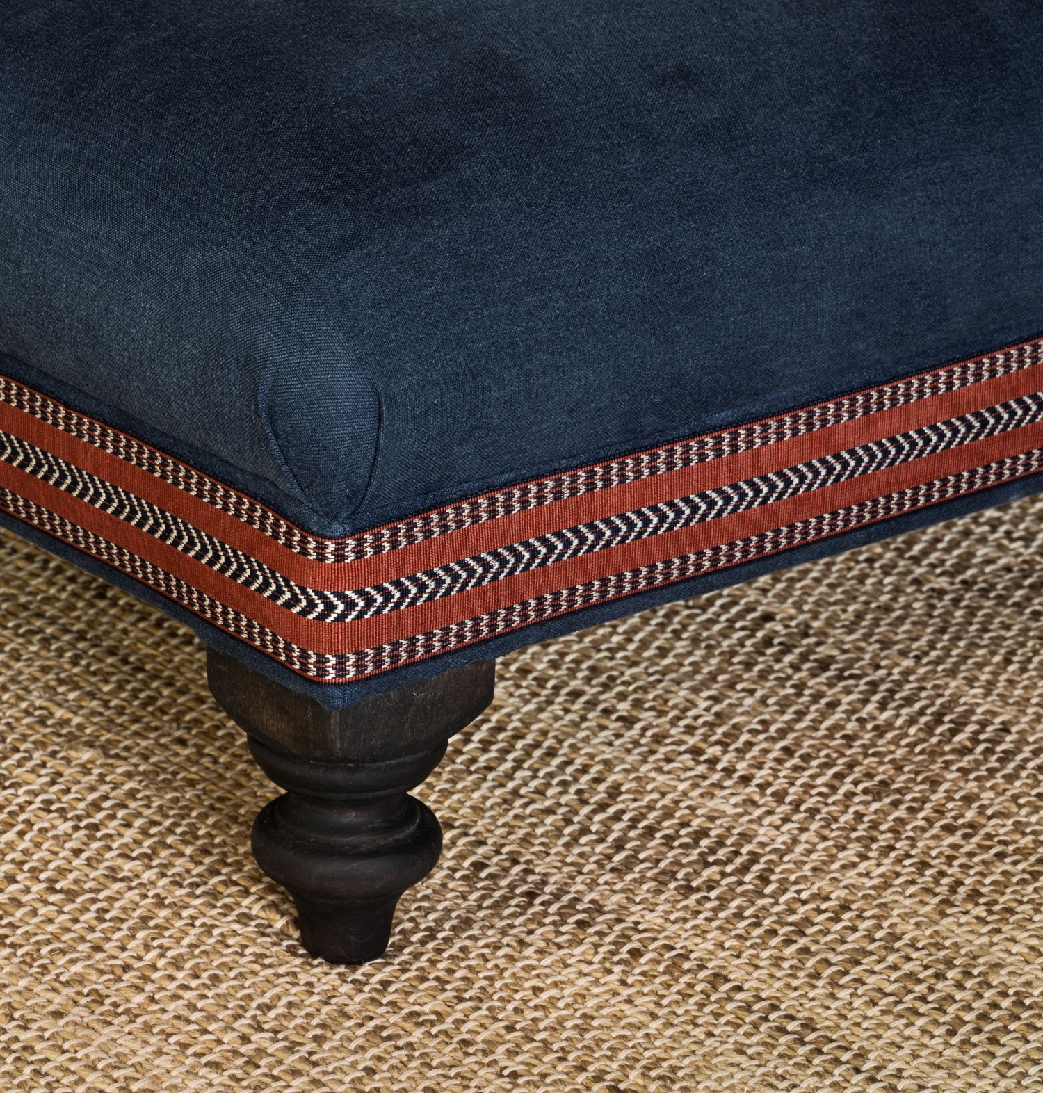 Collett & Victor Amber pouf in deep blue fabric with decorative trim and turned wooden leg.