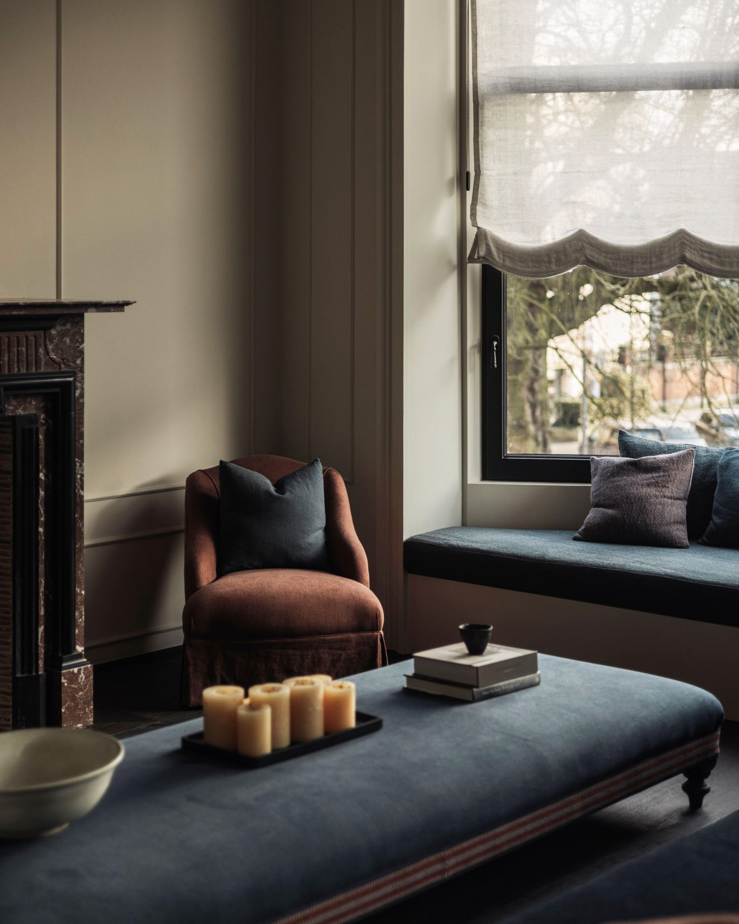 Cosy living room corner with upholstered Kitros armchair, Amber pouf and window seat in dark tones
