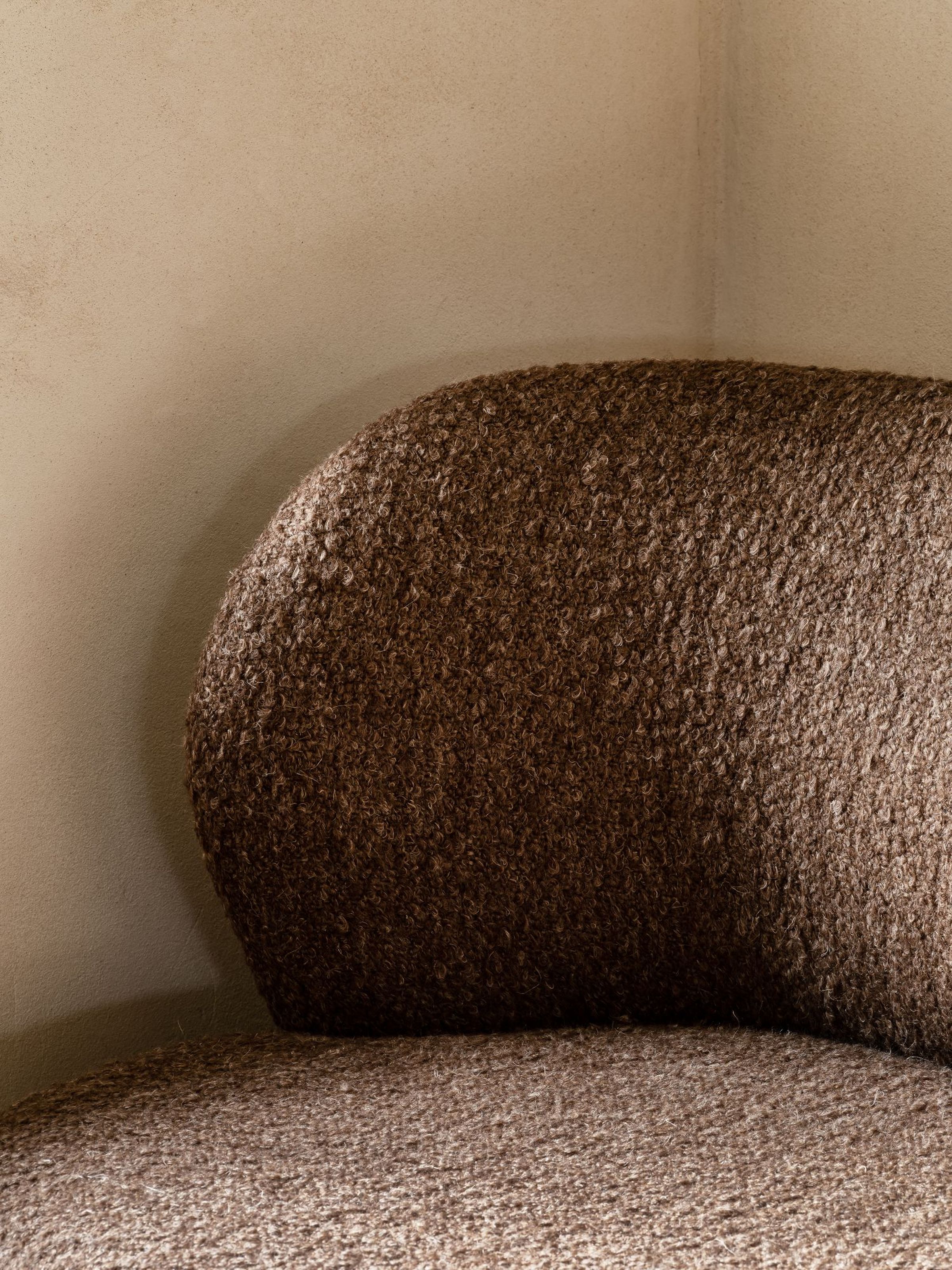 Close-up of the curved backrest and fabric texture of a brown loveseat in soft, warm light.