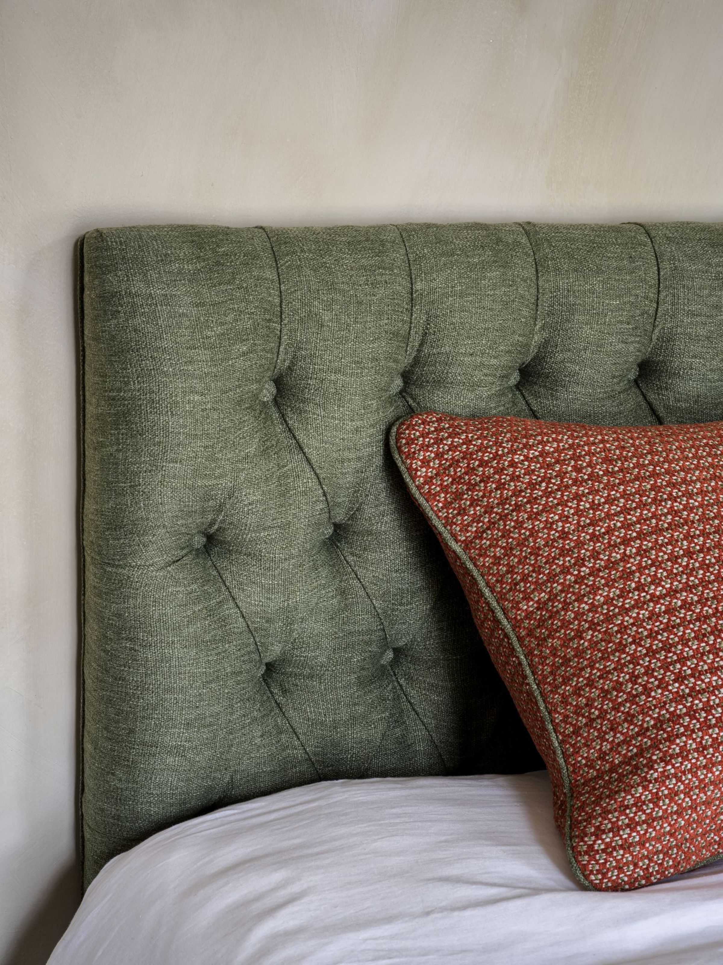 Collett & Victor Aurora headboard upholstered in textured green fabric with deep button tufting, styled with white bedding and red patterned cushion in a modern bedroom interior.
