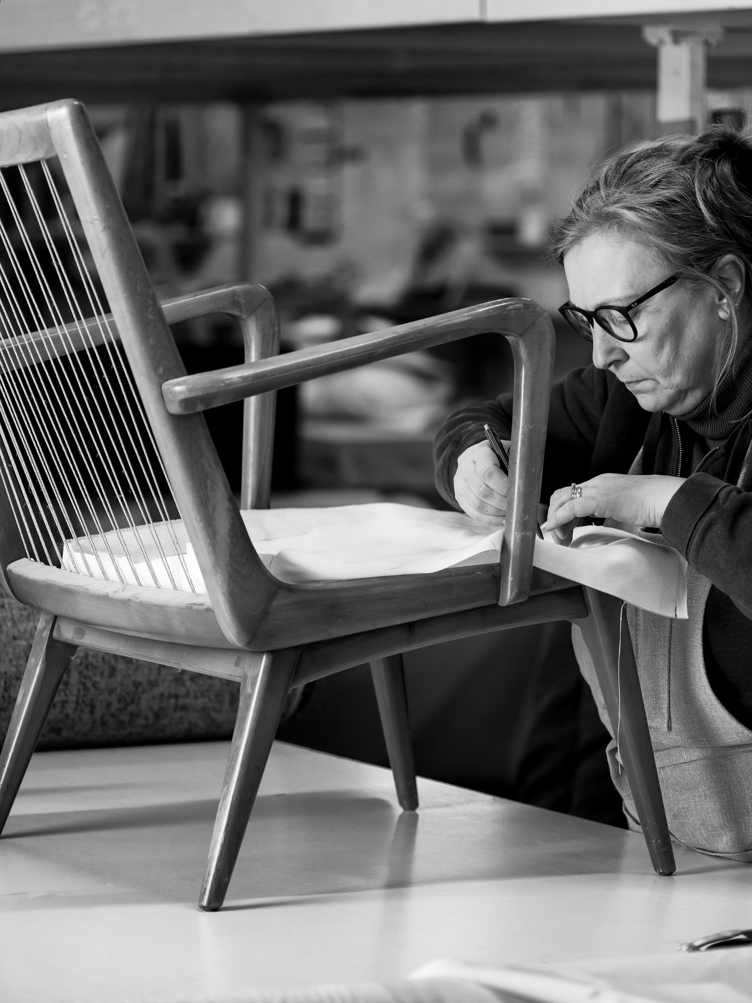 Craftswoman upholstering a wooden chair by hand in the Collett & Victor atelier – traditional furniture craftsmanship in black and white.