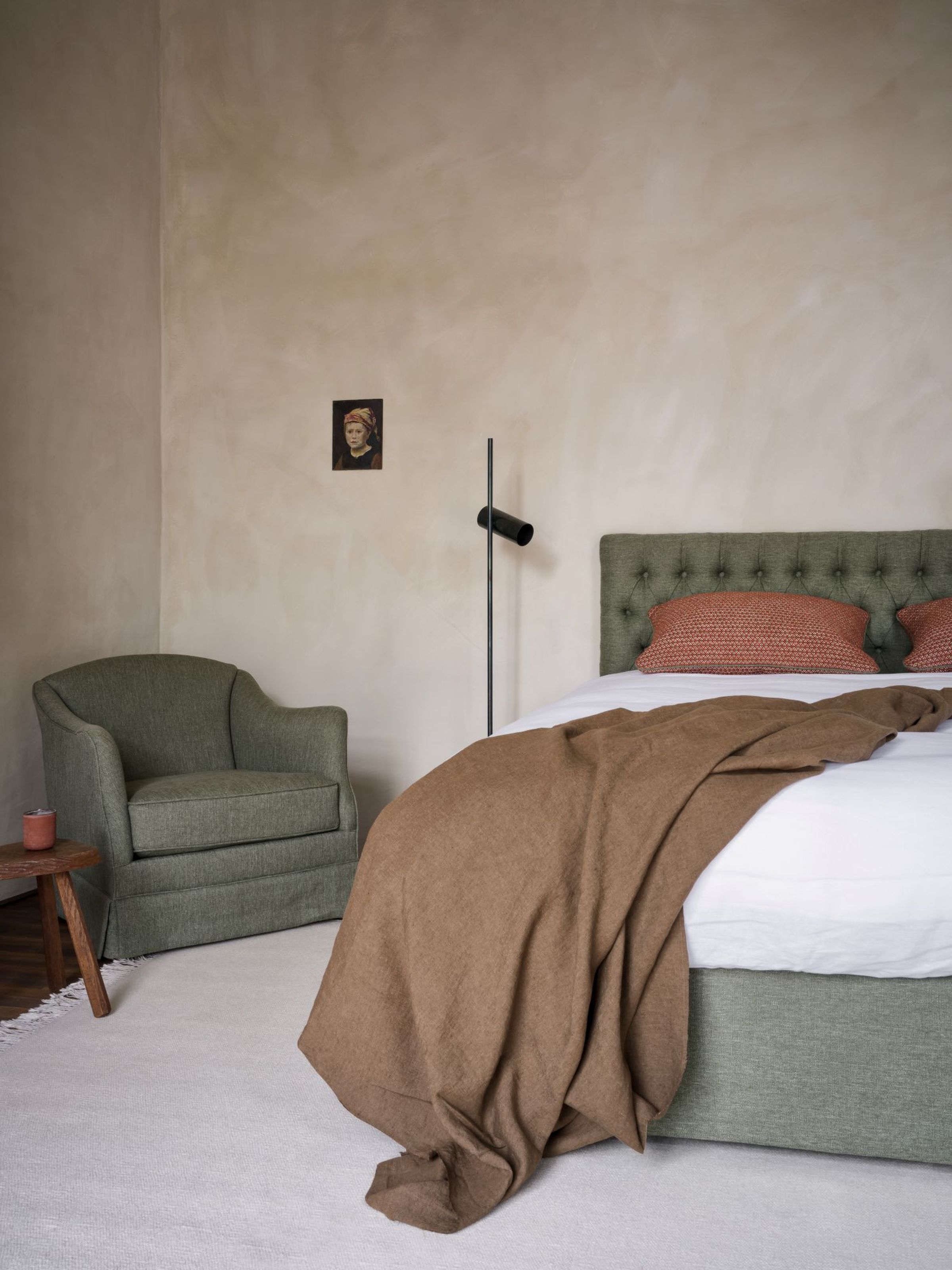 Collett & Victor Aurora bed with tufted green headboard and matching base, styled with rust cushions, brown linen throw and green armchair in a soft neutral bedroom interior.