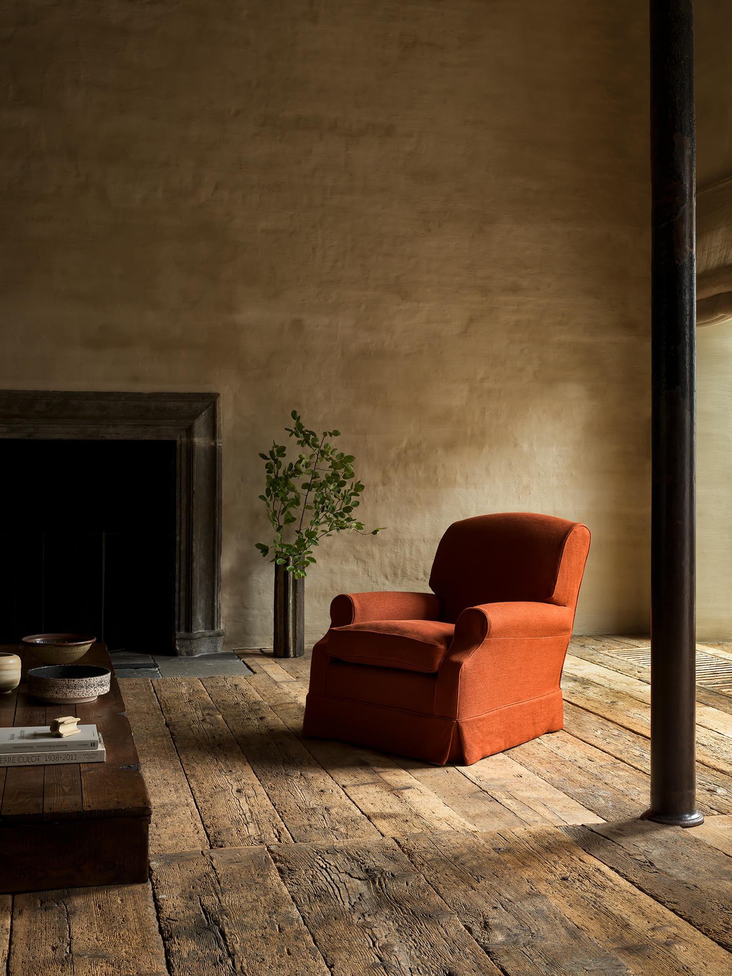 Joffre one-seater armchair in red upholstery showcased in rustic interior with wooden floor and neutral walls.