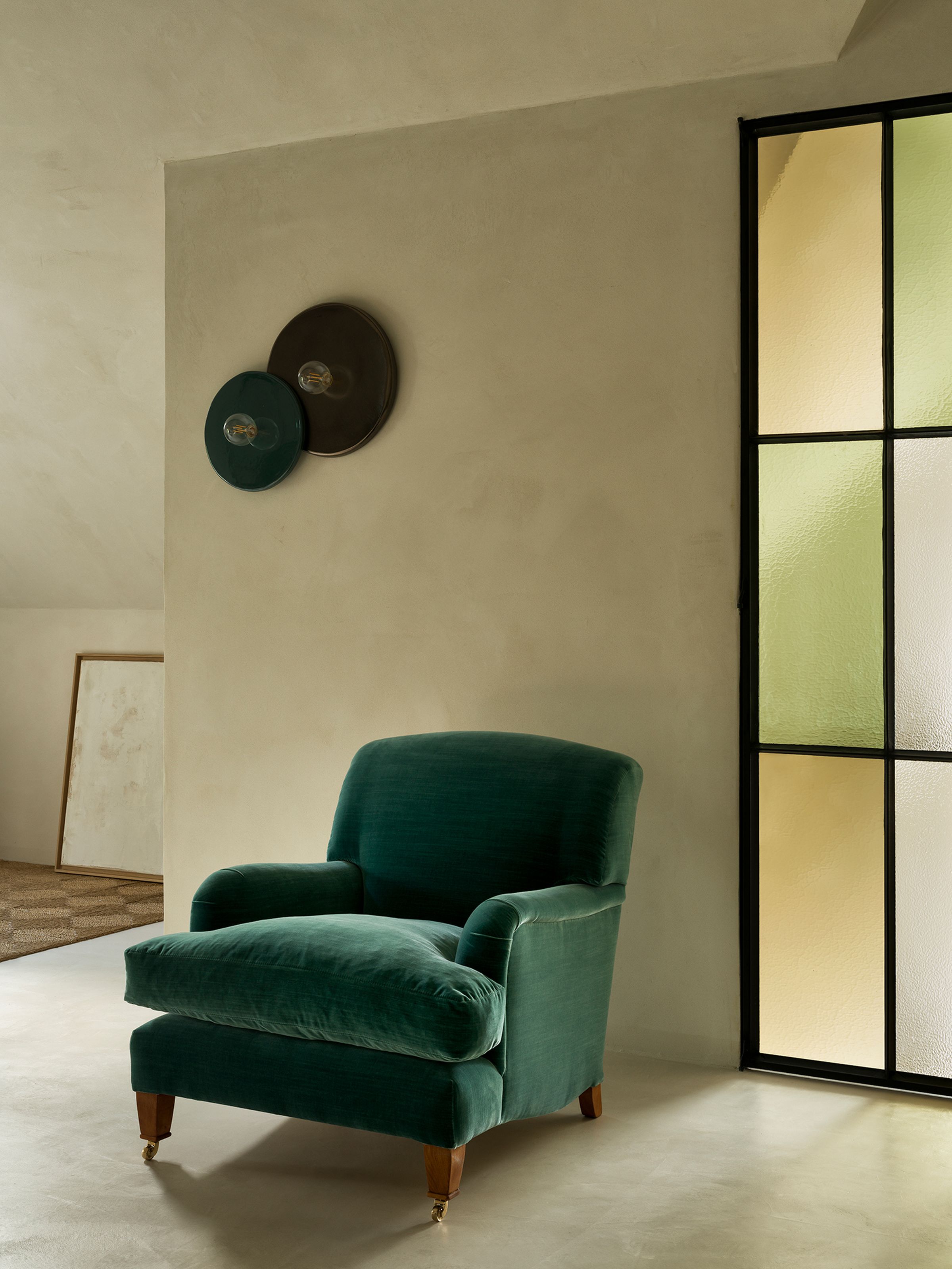 Hecto loose seat armchair in green velvet with wooden legs and brass casters in modern living room.