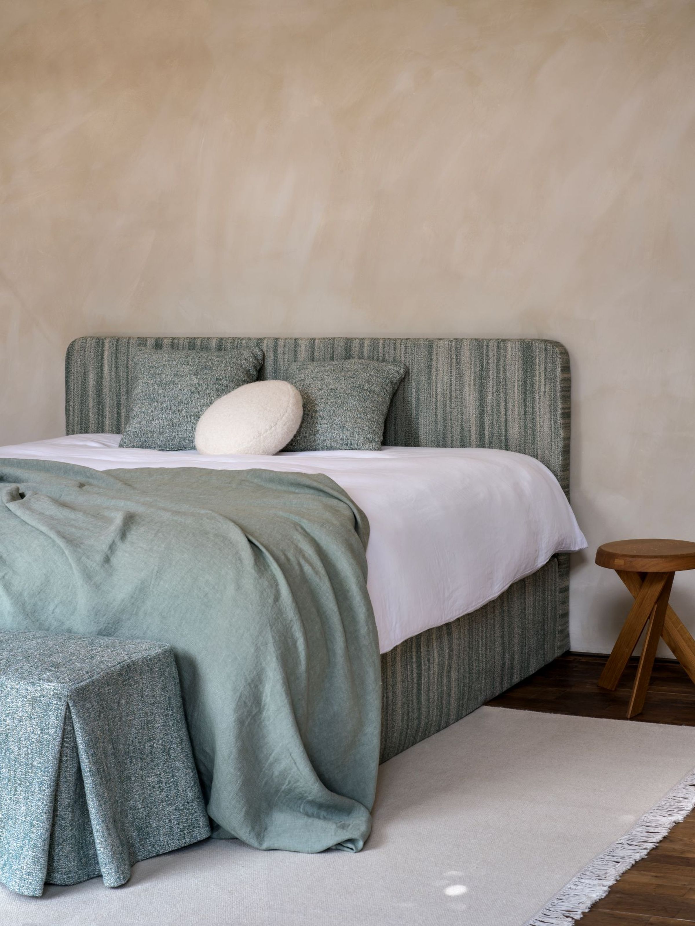 Bedroom with Claire headboard by Collett & Victor, upholstered in soft green striped fabric, styled with matching bed base, green throw, decorative cushions, and wooden side stool in a serene interior.