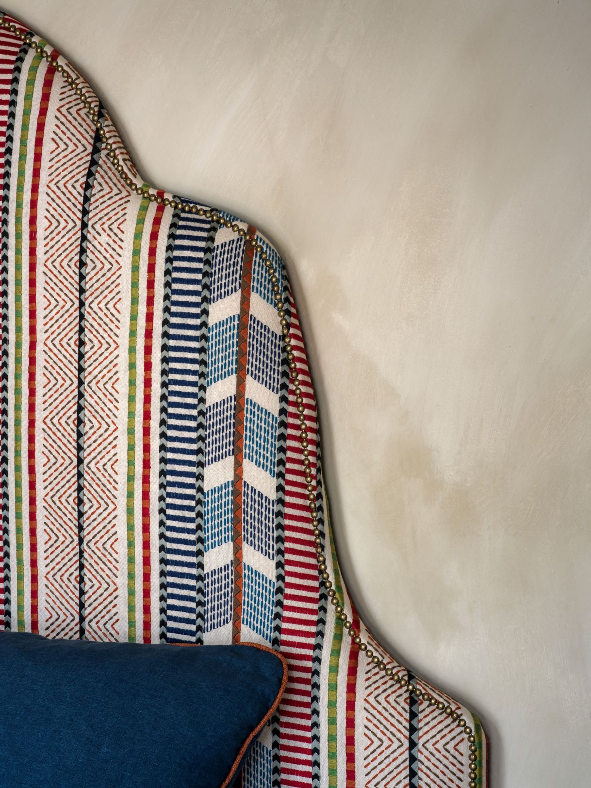 Close-up of the Penelope headboard by Collett & Victor, showcasing its arched silhouette, bold multicolored striped upholstery, and decorative brass nailhead trim along the edge.