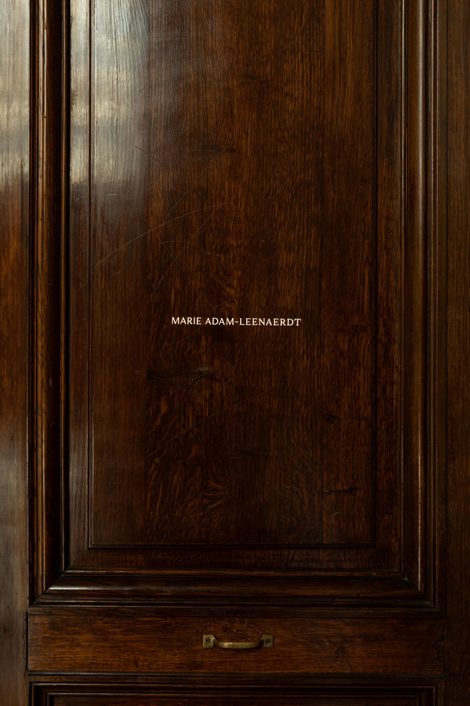 Close-up of a dark wooden paneled door with the name “Marie Adam-Leenaerdt” engraved in the center, adding a refined, classic detail.