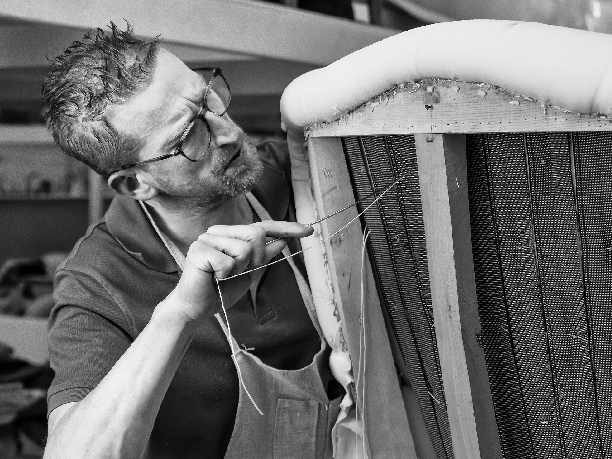 Collett & Victor craftsman hand-stitching upholstery on wooden furniture frame in atelier.